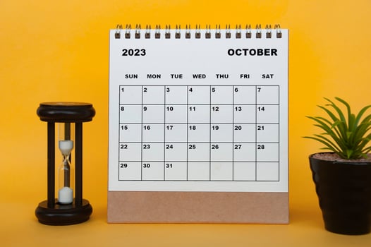 October 2023 desk calendar with minutes glass and plant on yellow background. photo