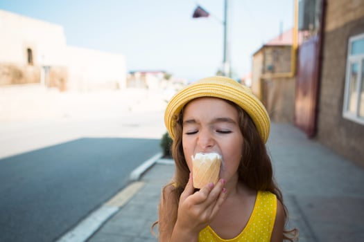 The child eats delicious ice cream outdoors with pleasure in the summer, soiled his mouth. A girl in a yellow hat and a sundress in the heat of a close-up portrait photo