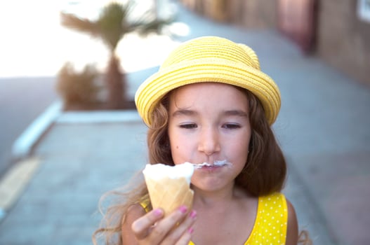 The child eats delicious ice cream outdoors with pleasure in the summer, soiled his mouth. A girl in a yellow hat and a sundress in the heat of a close-up portrait photo