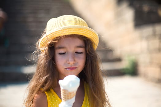 The child eats delicious ice cream outdoors with pleasure in the summer, soiled his mouth. A girl in a yellow hat and a sundress in the heat of a close-up portrait photo