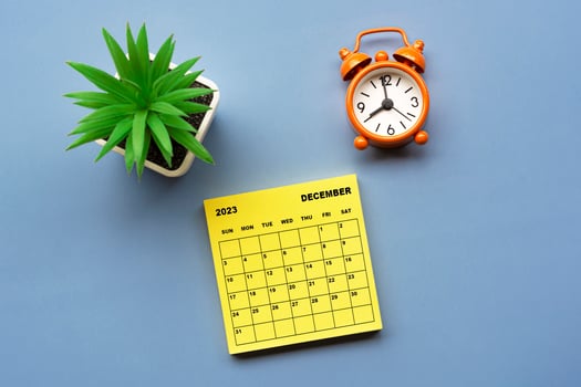 December 2023 calendar on adhesive note with alarm clock set at 8 o'clock. photo