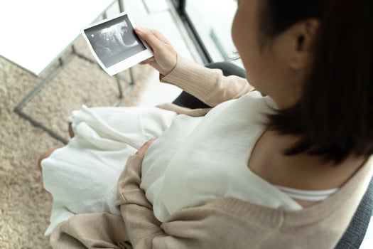 Asian pregnant woman looking at ultrasound picture at home photo
