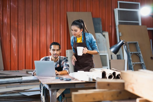 Young Asian couple carpenters man and woman discussing about design of products on laptop in woodcraft carpentry workshop. photo