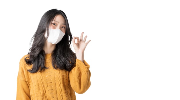 Asian young woman wears face mask and showing okay gesture on isolate white background photo