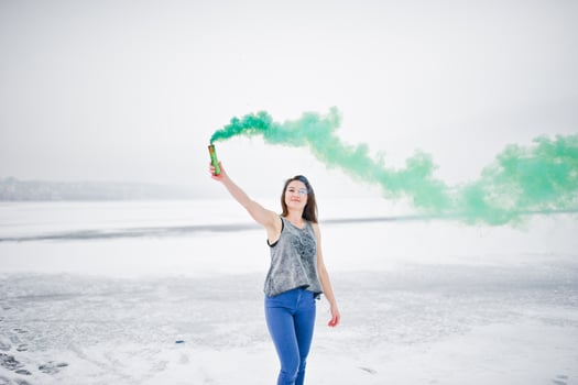 Young girl with green colored smoke bomb in hand in winter day. photo