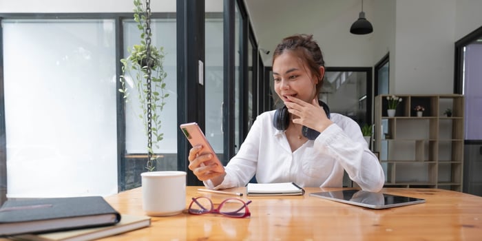 Happy young asian teen girl sit on sofa at home holding phone looking at screen waving hand video calling distance friend online in mobile chat app using smartphone videochat application. photo
