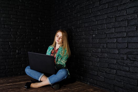Stylish blonde girl in jacket and jeans with laptop against brick black wall at studio. photo