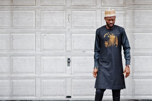 Rich african man in stylish traditional clothes and hat posed against garage gates. photo