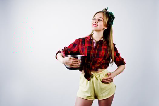 Young funny housewife in checkered shirt and yellow shorts pin up style with saucepan and kitchen spoon isolated on white background. photo