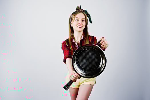 Young funny housewife in checkered shirt and yellow shorts pin up style with frying pan isolated on white background. photo