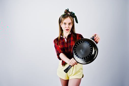 Young funny housewife in checkered shirt and yellow shorts pin up style with frying pan isolated on white background. photo