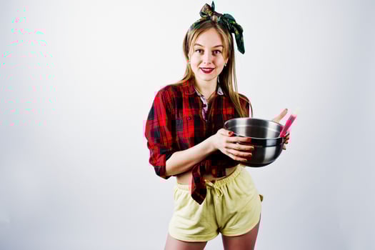 Young funny housewife in checkered shirt and yellow shorts pin up style with saucepan and kitchen spoon isolated on white background. photo