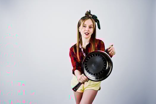 Young funny housewife in checkered shirt and yellow shorts pin up style with frying pan isolated on white background. photo