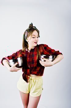 Young funny housewife in checkered shirt and yellow shorts pin up style with two saucepan isolated on white background. photo