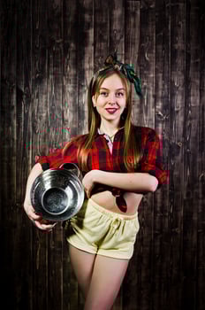 Young funny housewife in checkered shirt and yellow shorts pin up style with kitchen sieve on wooden background. photo