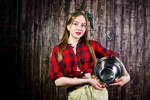 Young funny housewife in checkered shirt and yellow shorts pin up style with kitchen sieve on wooden background. photo