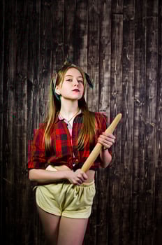 Young funny housewife in checkered shirt and yellow shorts pin up style with kitchen rolling pin on wooden background. photo