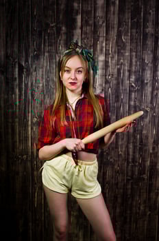 Young funny housewife in checkered shirt and yellow shorts pin up style with kitchen rolling pin on wooden background. photo