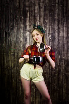 Young funny housewife in checkered shirt and yellow shorts pin up style with saucepan on wooden background. photo