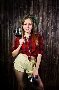 Young funny housewife in checkered shirt and yellow shorts pin up style with saucepan on wooden background. photo