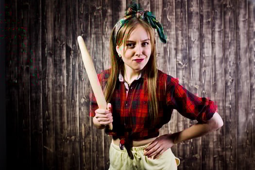 Young funny housewife in checkered shirt and yellow shorts pin up style with kitchen rolling pin on wooden background. photo