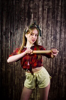 Young funny housewife in checkered shirt and yellow shorts pin up style with kitchen rolling pin on wooden background. photo
