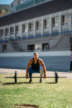 Young guy raises the bar in the stadium, outdoor workout photo