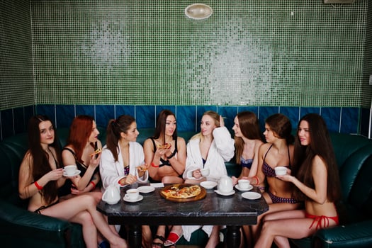 Group of eight sexy girls in swimsuits and bathrobe sitting in a bath and eating pizza. Girls rest friends. photo