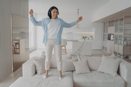 Excited energetic woman wearing headphones having fun enjoying music jumping on sofa alone at home photo