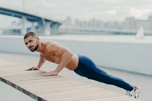 Full length shot of sporty muscular man in sportswear does push up exercise has concentrated serious expression poses outdoor. Self determined bearded sportsman planking for having strong arms photo