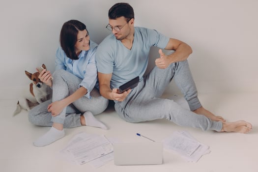 Photo of satisfied man wears spectacles and casual clothes, shows figures on calculator, demonstartes okay gesture, rejoices high profits, works together with female colleague, sit on floor.