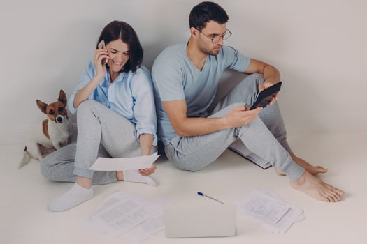 Young woman and man sit back to each other, do accounts together, make necessary calculations, surrounded with paper documents, sit on floor in empty room with dog. People and finances concept photo