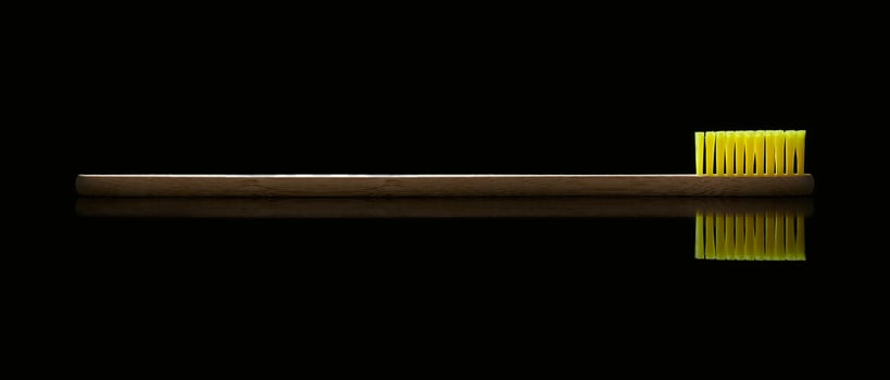 Natural bamboo toothbrush with yellow bristles on black isolated background. Oral care and dental health. Photo with copy space.
