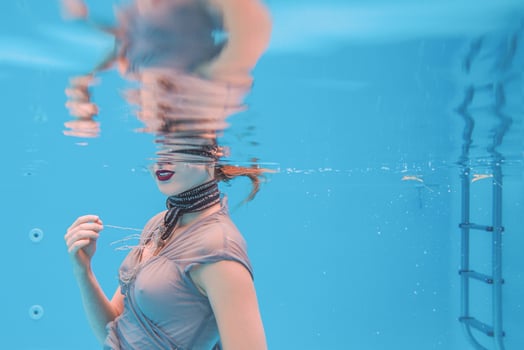 surreal art portrait of young woman in grey dress and beaded scarf underwater in the swimming pool photo