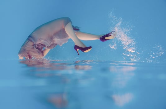 surreal art portrait of young woman in grey dress, beaded scarf , small bag, violet high heels  underwater in the swimming pool photo