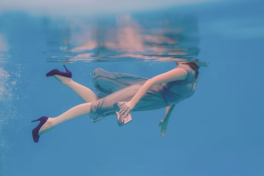 surreal art portrait of young woman in grey dress, beaded scarf, small bag, violet high heels  underwater in the swimming pool photo