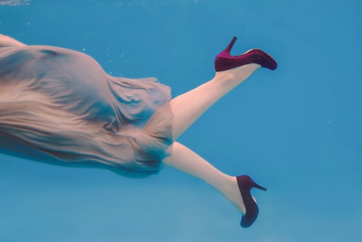 surreal art portrait of young woman in grey dress, beaded scarf , small bag, violet high heels  underwater in the swimming pool photo