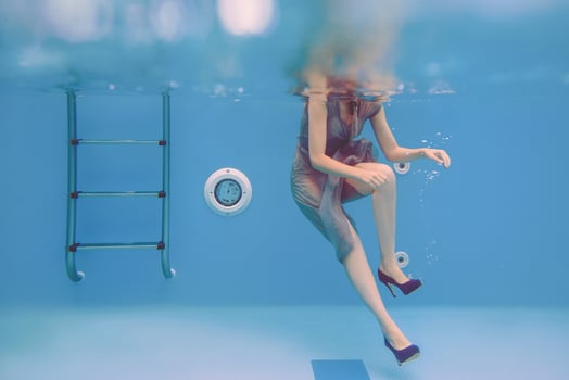 surreal art portrait of young woman in grey dress, beaded scarf , small bag, violet high heels  underwater in the swimming pool photo