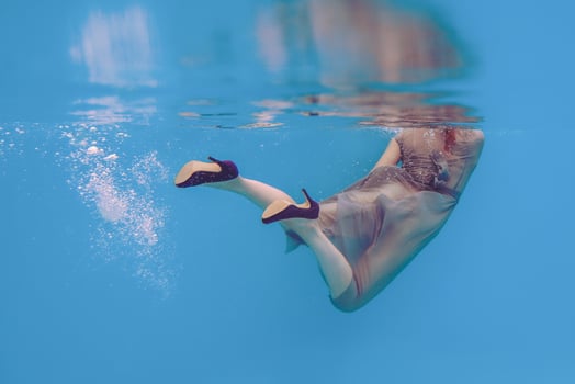 surreal art portrait of young woman in grey dress, beaded scarf , small bag, violet high heels  underwater in the swimming pool photo