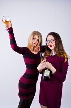Two attractive friends in purple dresses drink sparkling wine or champagne in the studio. photo
