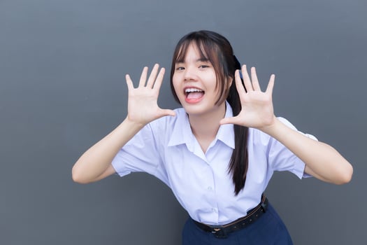 Beautiful Asian high school student girl in the school uniform with smiles confidently while she looks at the camera happily with grey in the background. photo