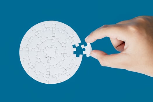 Close up hand holding and playing jigsaw game incomplete. White part of jigsaw puzzle pieces on blue background. concepts of problem solving, business, teamwork, Texture photo with copy space for text