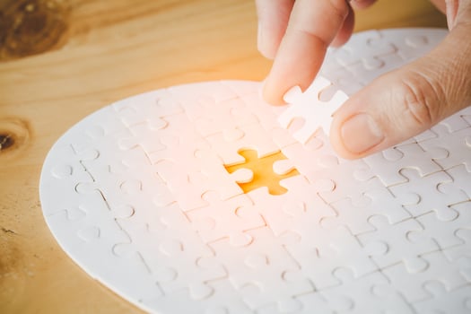 Close up hand holding and playing jigsaw game incomplete. White part of jigsaw puzzle pieces on table background. concepts of problem solving, business, teamwork. photo