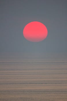 The sun is falling into the sea and being partially swallowed by the fog.  sky  is dark photo