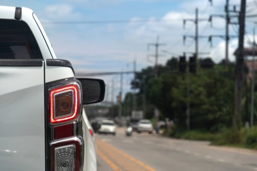 Back side of pick up car white color on the asphalt road. Turn on brake light. with blurred background of other cars far away. with trees and green grass beside road. photo