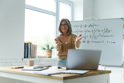 Happy senior woman gesturing while standing near the whiteboard at classroom photo