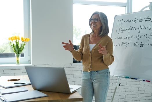 Confident senior woman gesturing and smiling while standing near the whiteboard at classroom photo