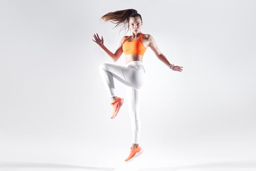 Beautiful young woman in sports clothing jumping against white background photo
