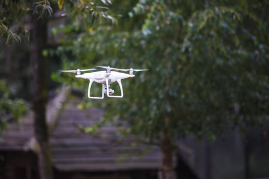 White flying quadrocopter with camera on green forest background photo