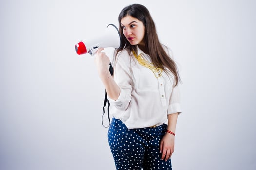 Portrait of a young woman in blue trousers and white blouse posing with megaphone in the studio. photo